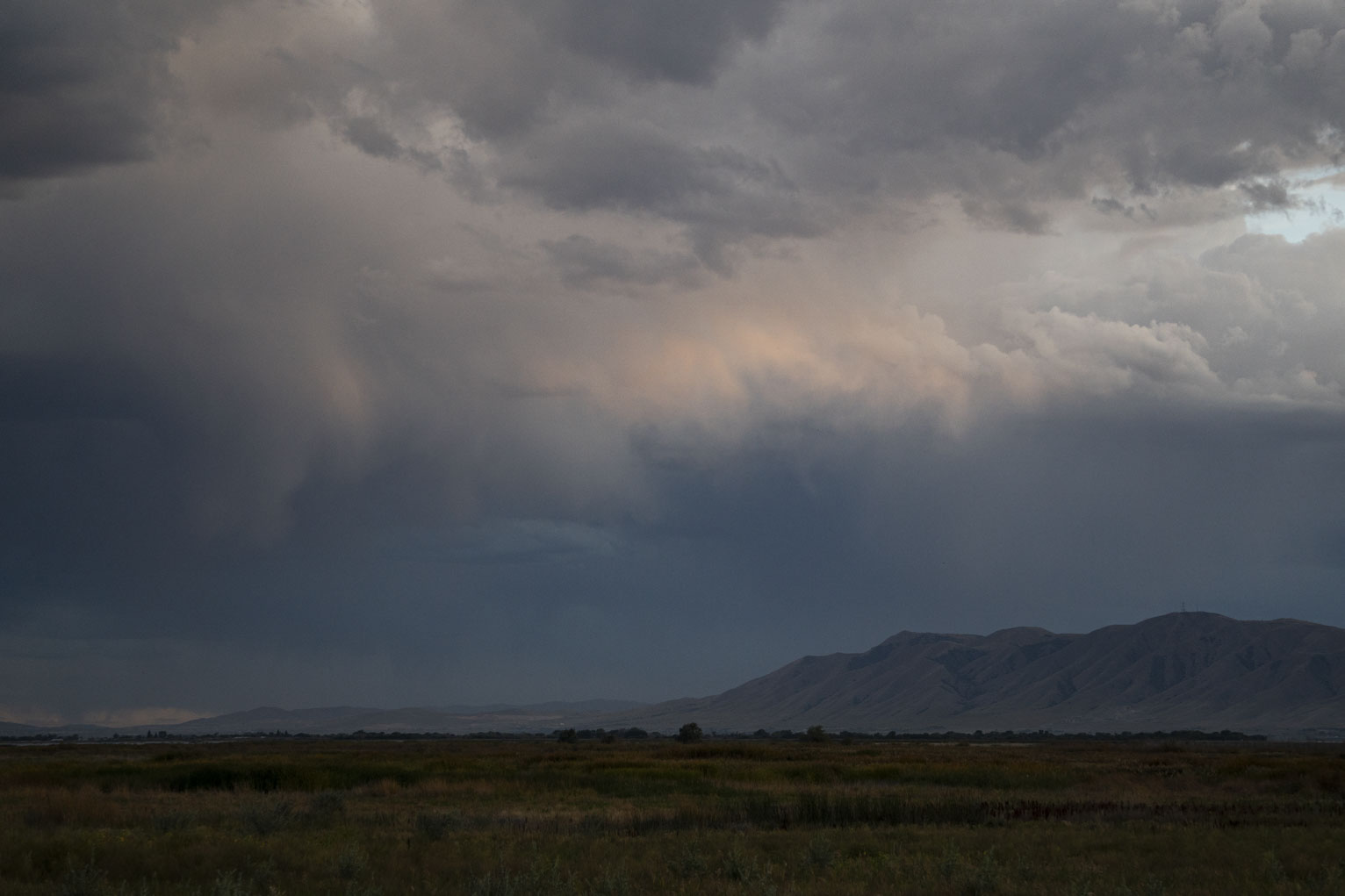 Rain sweeps over teh west mountains beyond fields